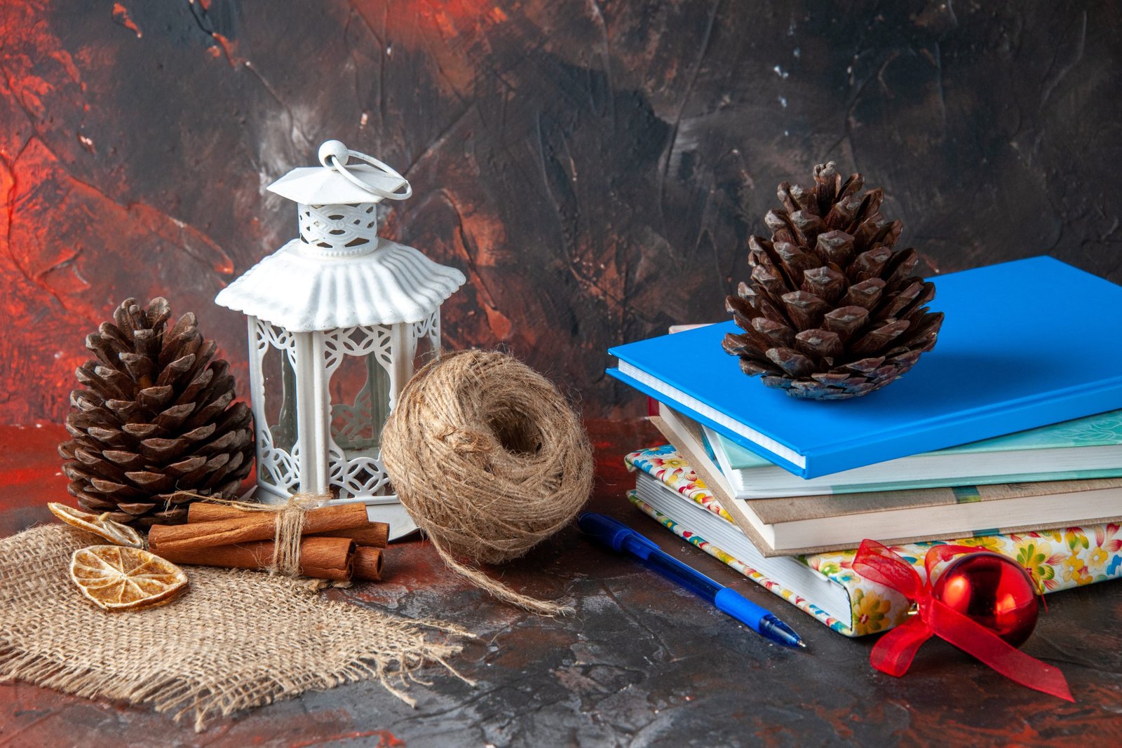 horizontal-view-stacked-notebooks-pen-ball-rope-cinnamon-limes-conifer-cones-dark-background